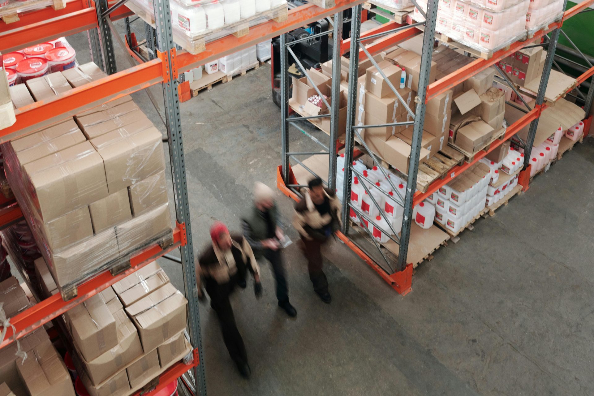 Vista desde un ángulo elevado de trabajadores en movimiento en un almacén ajetreado con estanterías llenas de cajas y paquetes.