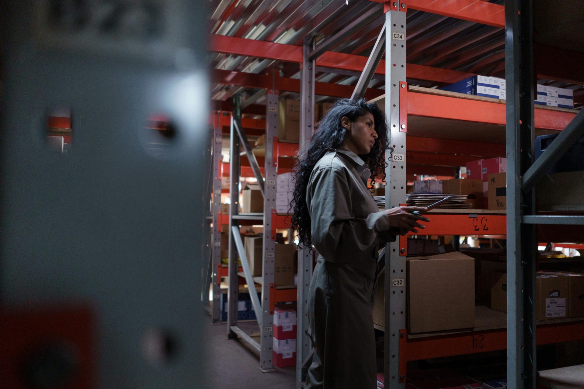Una mujer adulta uniformada revisando el inventario en un pasillo de un almacén.