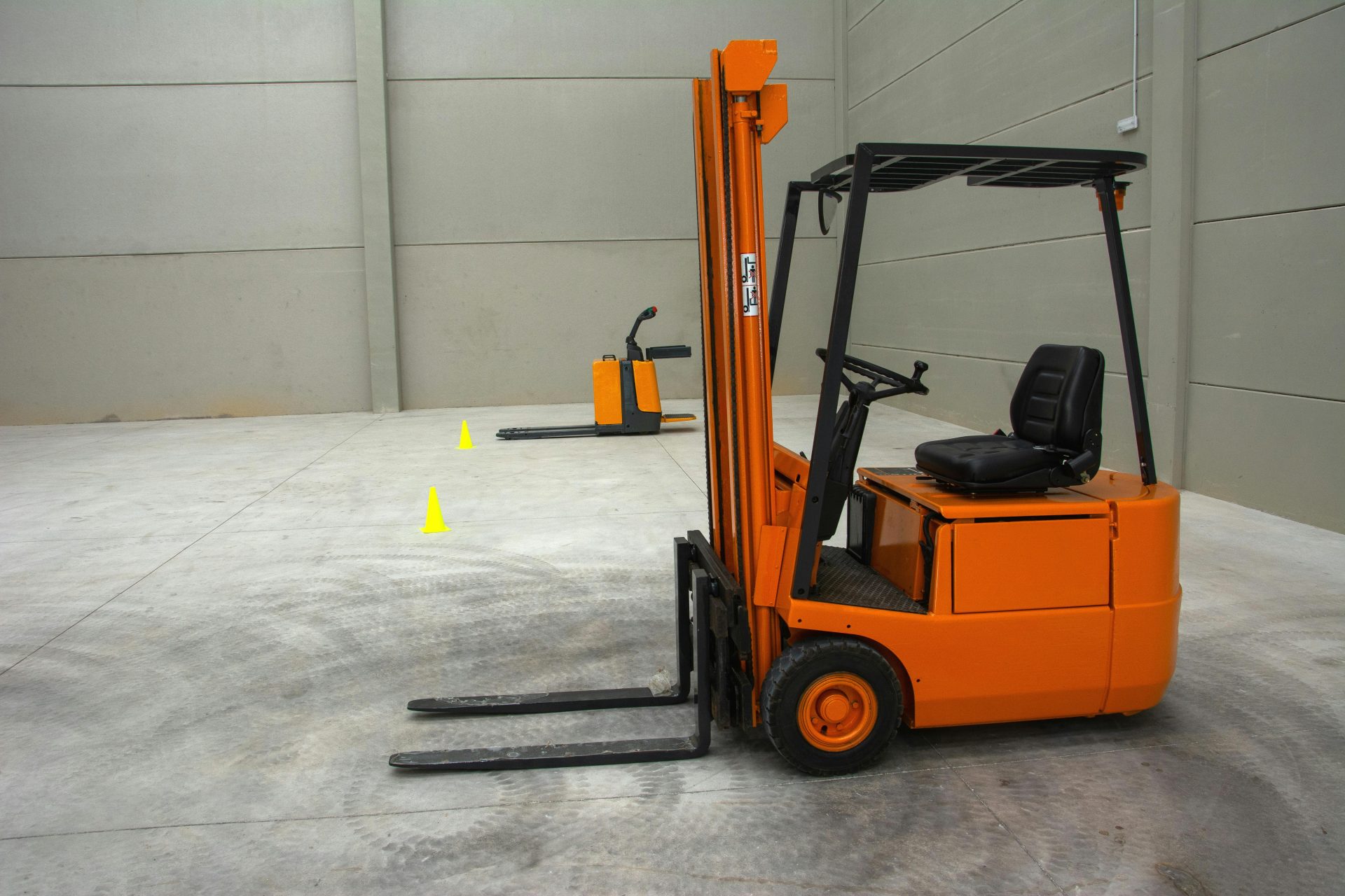 Una carretilla elevadora naranja en un amplio almacén con suelos de hormigón y equipamiento mínimo.